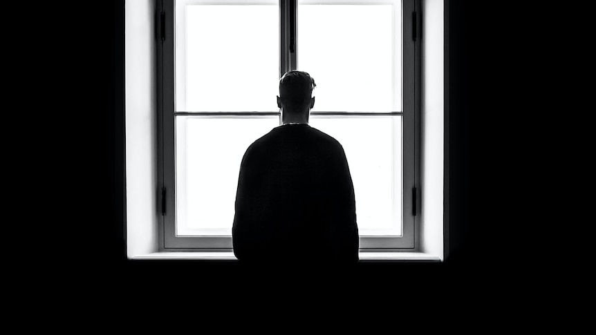 Silhouette of person with short hair standing against a large window with clear expanse.