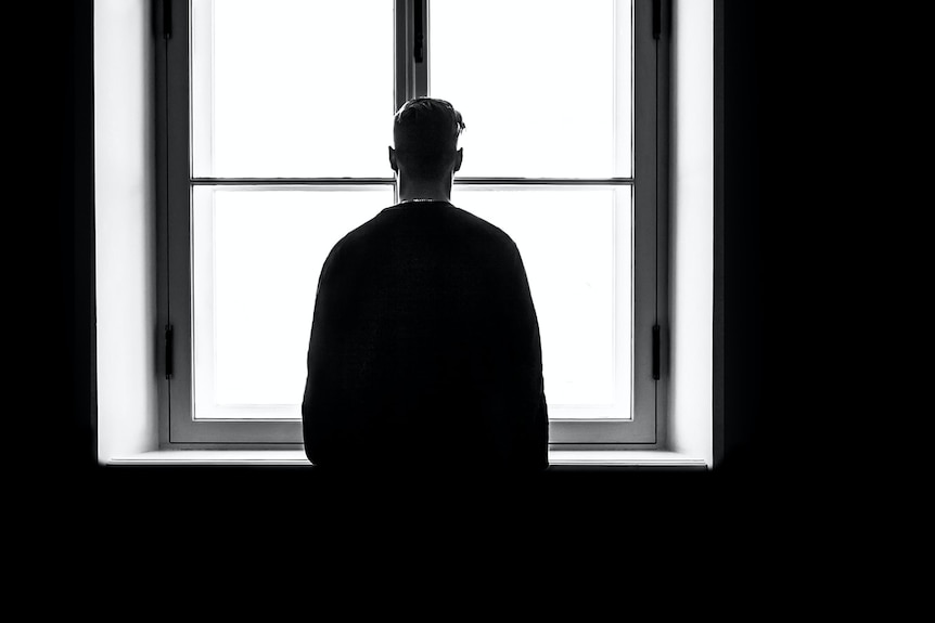 Silhouette of person with short hair standing against a large window with clear expanse.