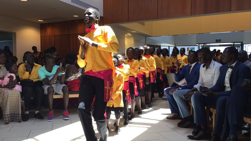 A line of Sudanese migrants wearing yellow outfits dance during a Christmas service.