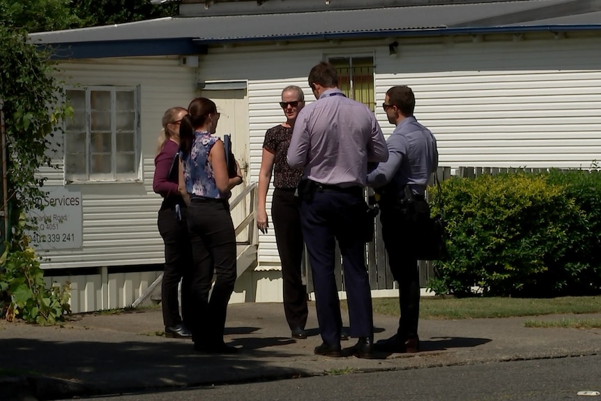 A group of people stand on a driveway talking to each other