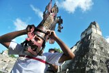 A member of a folklore group places a mask on his head in front of the Mayan Gran Jaguar temple in Guatemala.