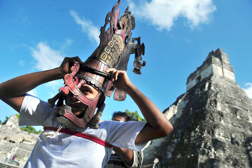 A member of a folklore group places a mask on his head in front of the Mayan Gran Jaguar temple in Guatemala.