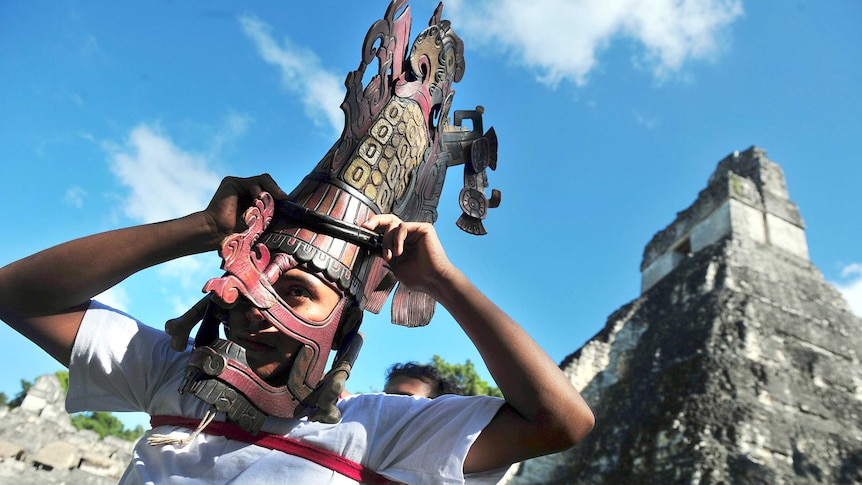 A member of a folklore group places a mask on his head in front of the Mayan Gran Jaguar temple in Guatemala.