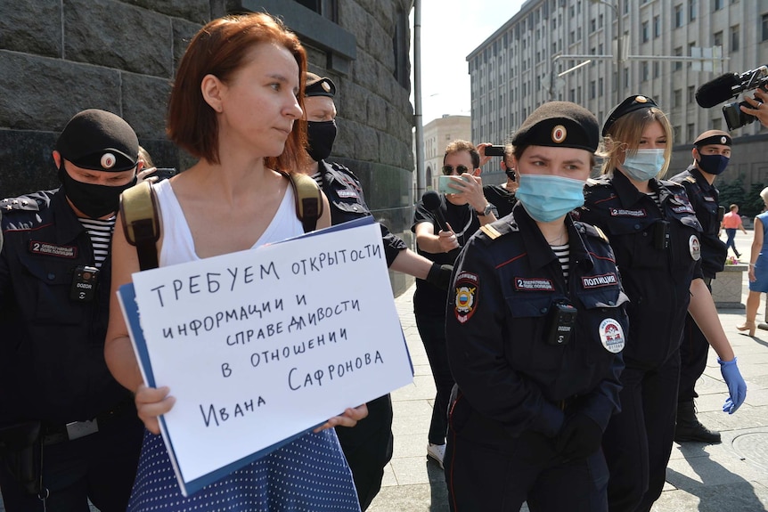 Russian police officers stand around a woman holding a handwritten sign in Russian .