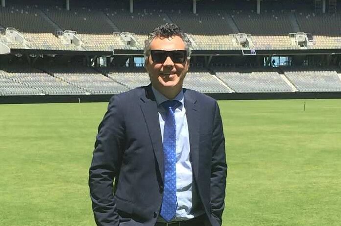 A man in a suit and sunglasses stands in the middle of Perth Stadium.