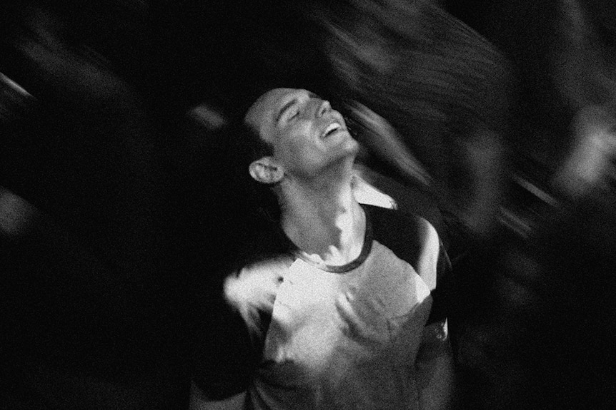 A black and white close-up still of Cory Michael Smith throwing his head back on dance floor in the 2018 film 1985.
