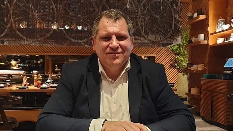 A man in a blue suit and white open necked shirt sits in a restaurant smiling