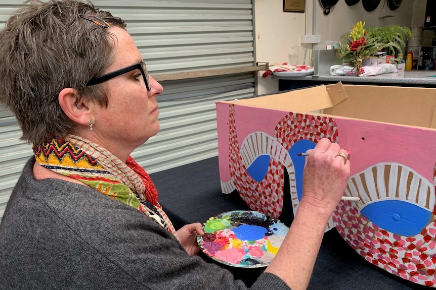 A woman paints a cardboard coffin in bright colours.