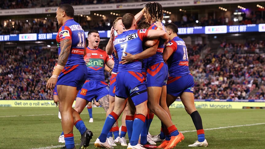 A group of Newcastle Knights NRL players embrace as they celebrate a try.
