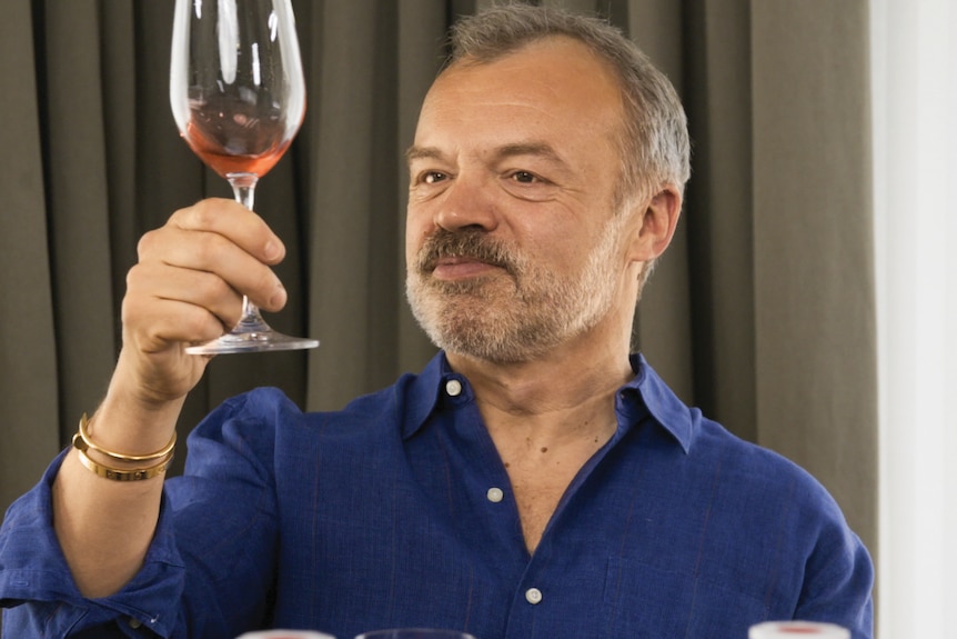 Comedian Graham Norton holding a glass of wine from the latest vintage of his own range of wines.