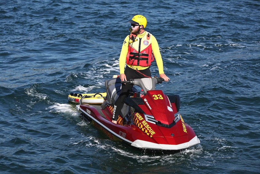 A surf rescue jet ski rider looks out over the water as he searches the ocean for a shark attack victim.