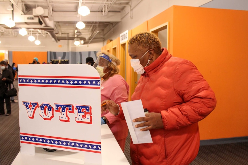 A woman in a face mask stands at a polling booth