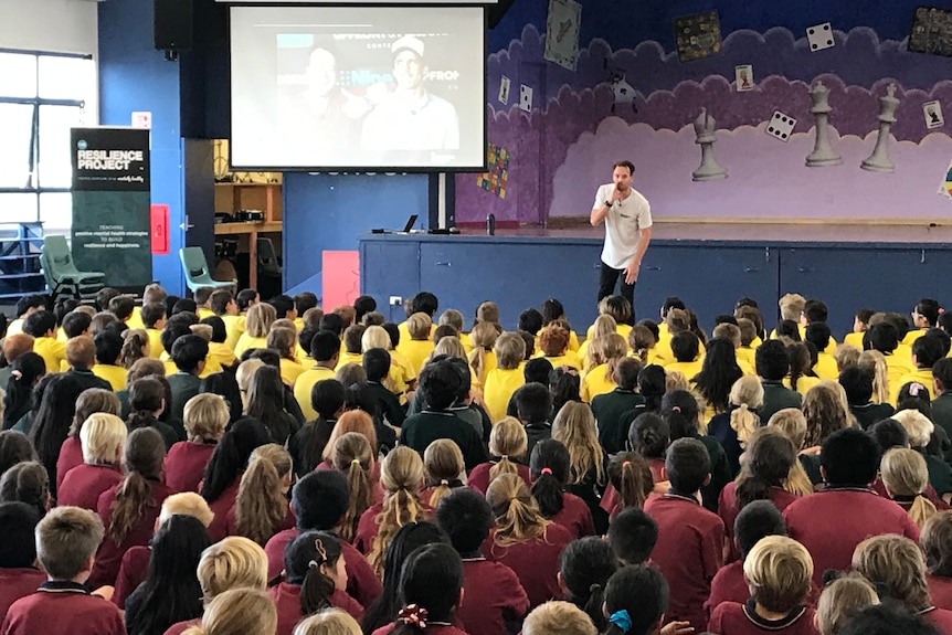 A man presents to a hall of school students in uniform