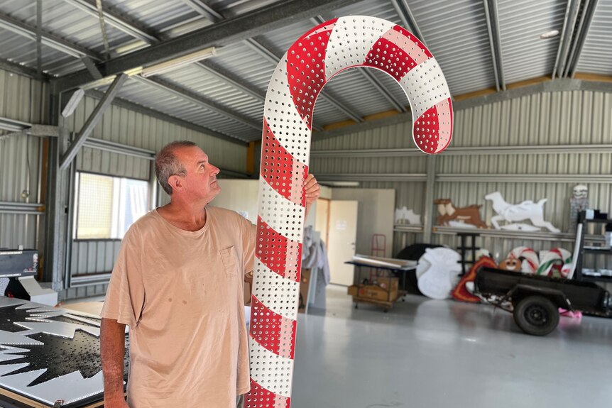 A man in a light pink shirt looks up at the giant candy cane he is holding