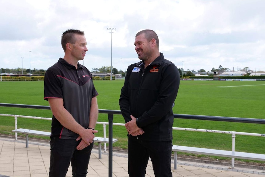 Two men stand in front of a football field