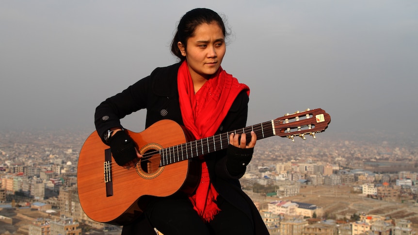 Shukria Hameedi plays classical guitar on a hill outside of Omid-e-Sabz Town.