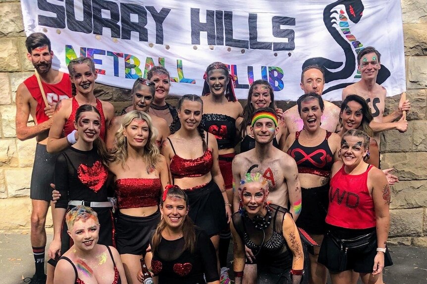 People stand together in a group wearing red and black, in front of a sign that says Surry Hills Netball Club