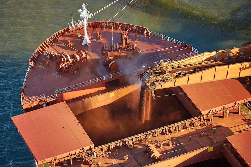 Aerial image of iron ore being loaded into a bulk carrier at a port.