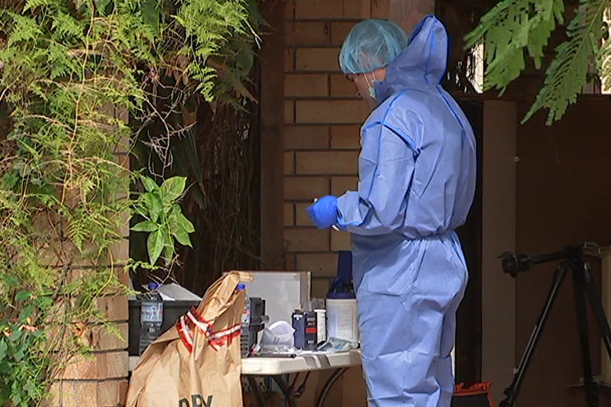 Man in a blue HAZMAT suit standing in front of a house