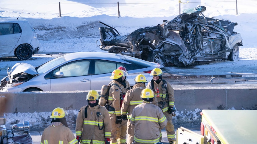 Emergency crews look on as a crumpled car's chassis sits on a snowy highway