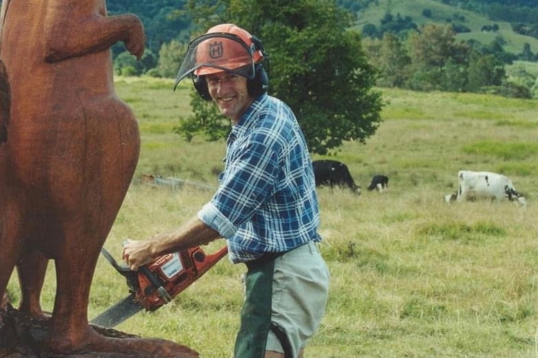 A man stands with a chainsaw next to a stump