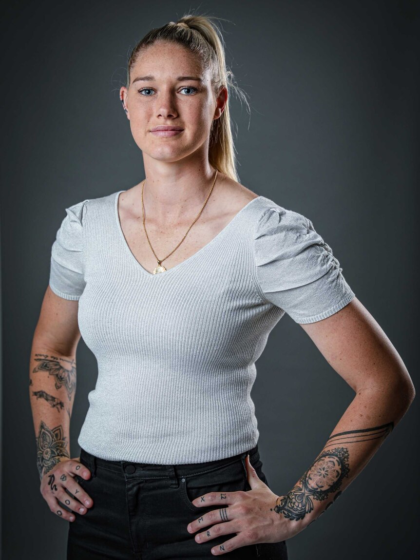A woman with tattoos on her forearms stands with hands on her hips.