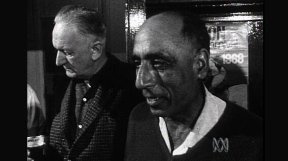 A Sikh man stands in the pub beside another man