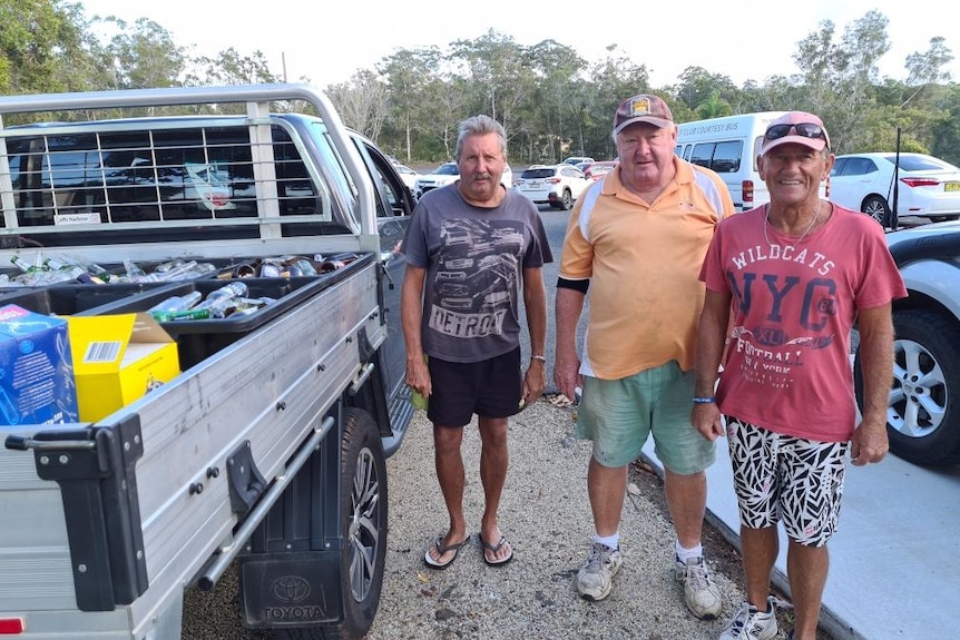 Three older men standing next to a ute filled with bottles to recycle.