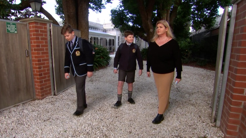 A woman walking down a driveway with two boys in school uniform