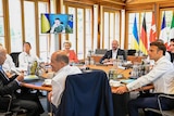 G7 leaders sitting around a table with the Ukrainian president on a monitor in the background.