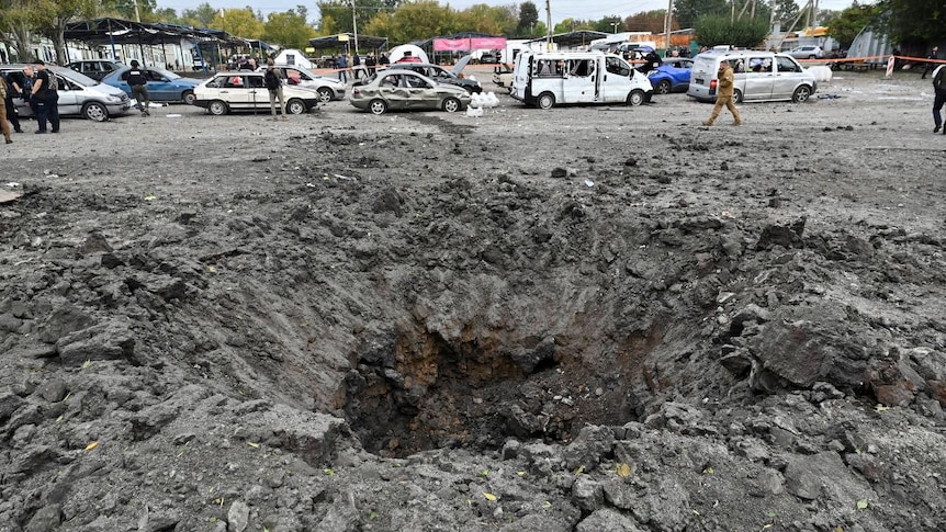 a crater can be seen in a road in Ukraine with people and cars parked behind it