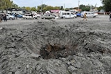 a crater can be seen in a road in Ukraine with people and cars parked behind it