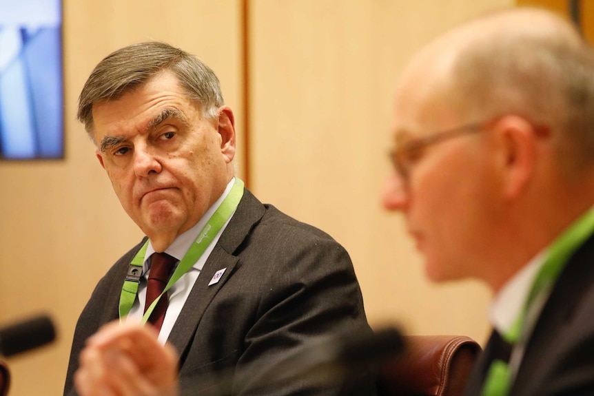 A man looks at another man in a committee hearing