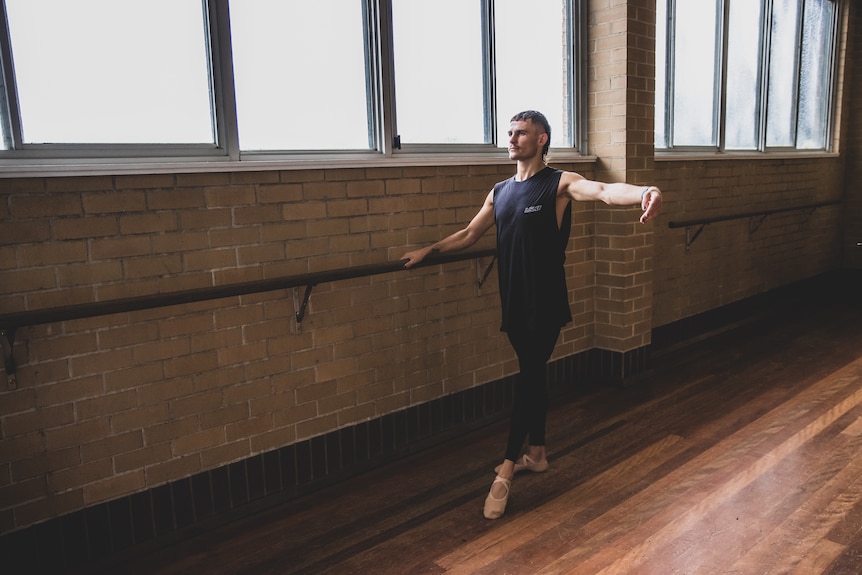 Harry Garside warms up at a ballet barre holding his arm in second position. 