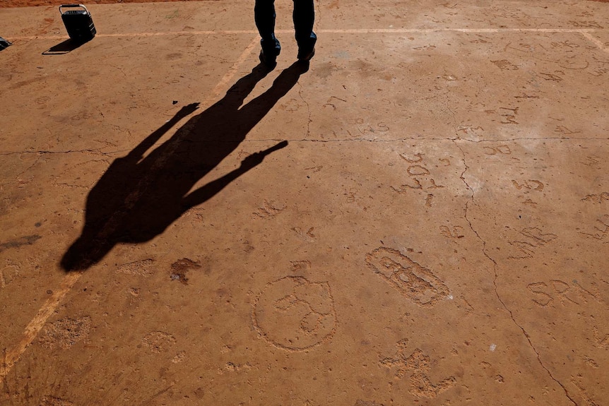 A shadow of Lance McDonald on a basketball court floor with markings carved into the concrete.