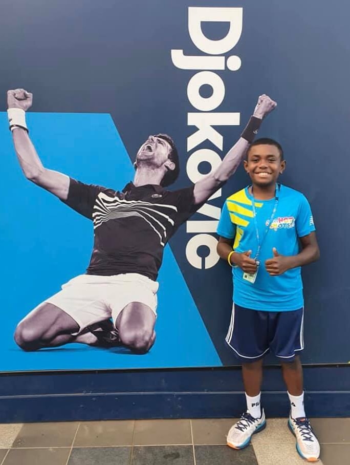 A 10-year-old boy gives the thumbs up in front of a poster of Novak Djokovic