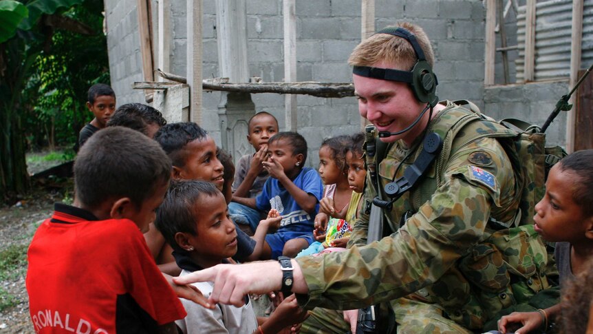 Children gather around an armed peacekeeper to play and talk to him