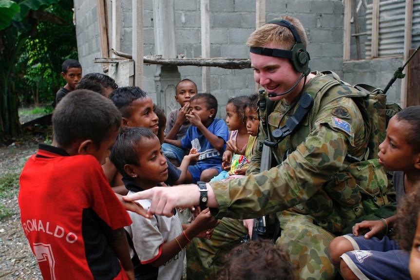 Children gather around an armed peacekeeper to play and talk to him