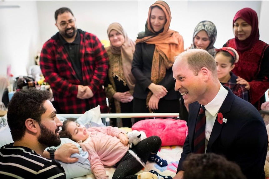 Prince William talks to a man next to a hospital bed with a small girl in it