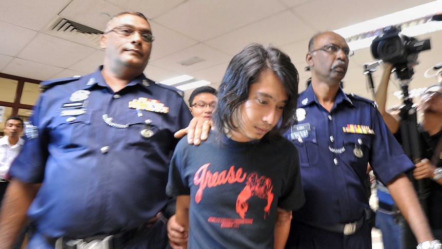 Malaysian police officers escort student activist Adam Adli Halim.