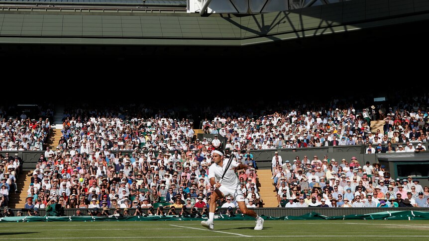 Roger Federer sets up for a back hand return shot as the crowd watches on in the Wimbledon sun