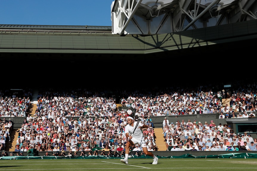 Roger Federer sets up for a back hand return shot as the crowd watches on in the Wimbledon sun
