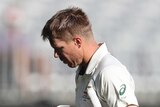 David Warner looks at his helmet as he carries it while trudging off after a dismissal