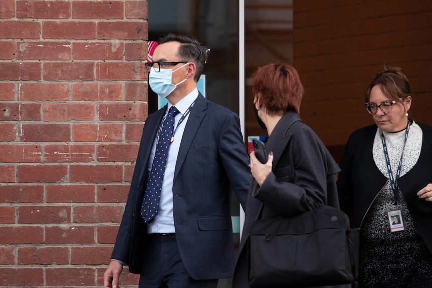 Tim Bullard leaves a building, flanked by two women.