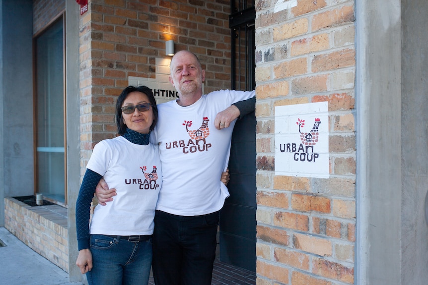 A man and woman in "Urban Coup" T-shirts outside an apartment building.