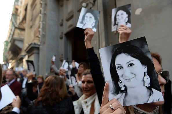 A crowd of people outside a church hold up photographs of Daphne Caruana Galizia