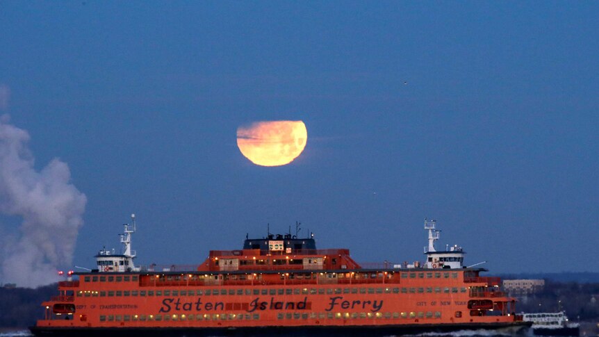 The "Super Blue Blood Moon" sets behind the Staten Island Ferry in New York.