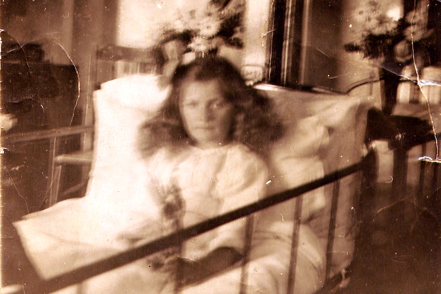 little girl sits in hospital bed, not smiling.  Photo is blurred, black and white image.