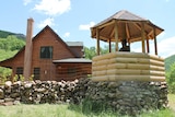 A man stands in a gazebo holding a gun as he looks out over the grass.