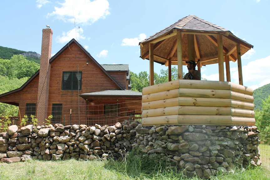 A man stands in a gazebo holding a gun as he looks out over the grass.